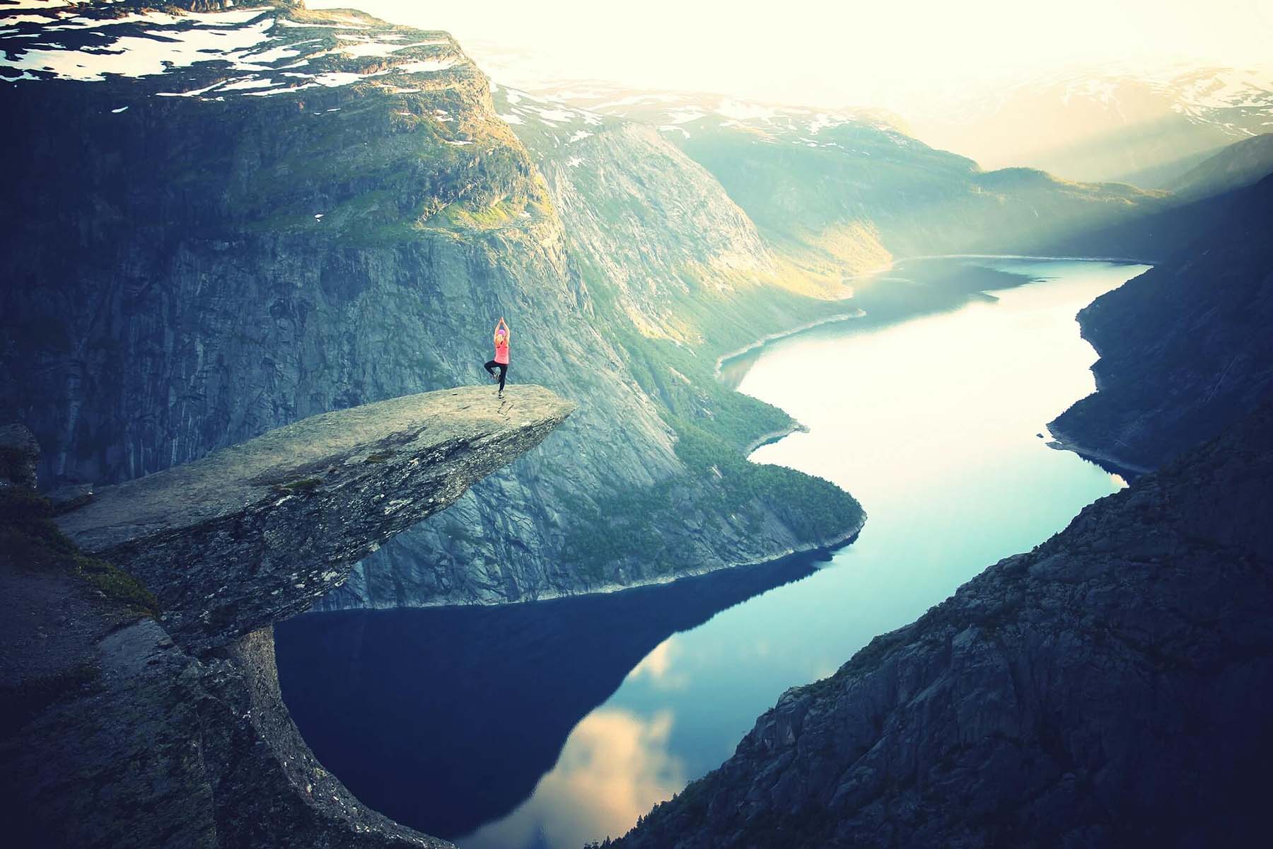 Woman doing YOGA on cliff stone looking over a mountain and a lake